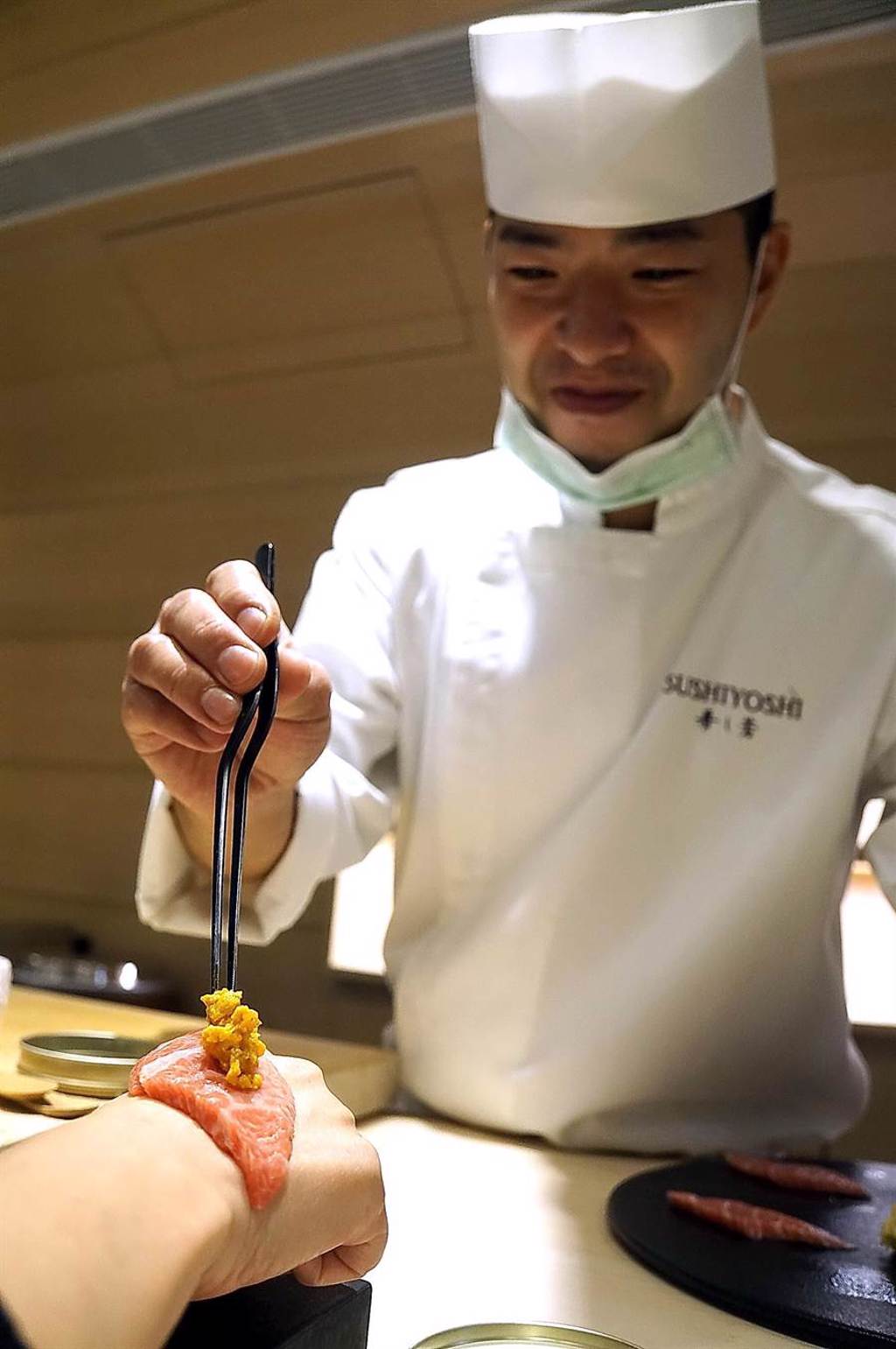 橋本和宏在客人手背上「料理」，將大閘蟹膏放在鮪魚大腹上再捲起，這當然需要點技術。（圖／姚舜）