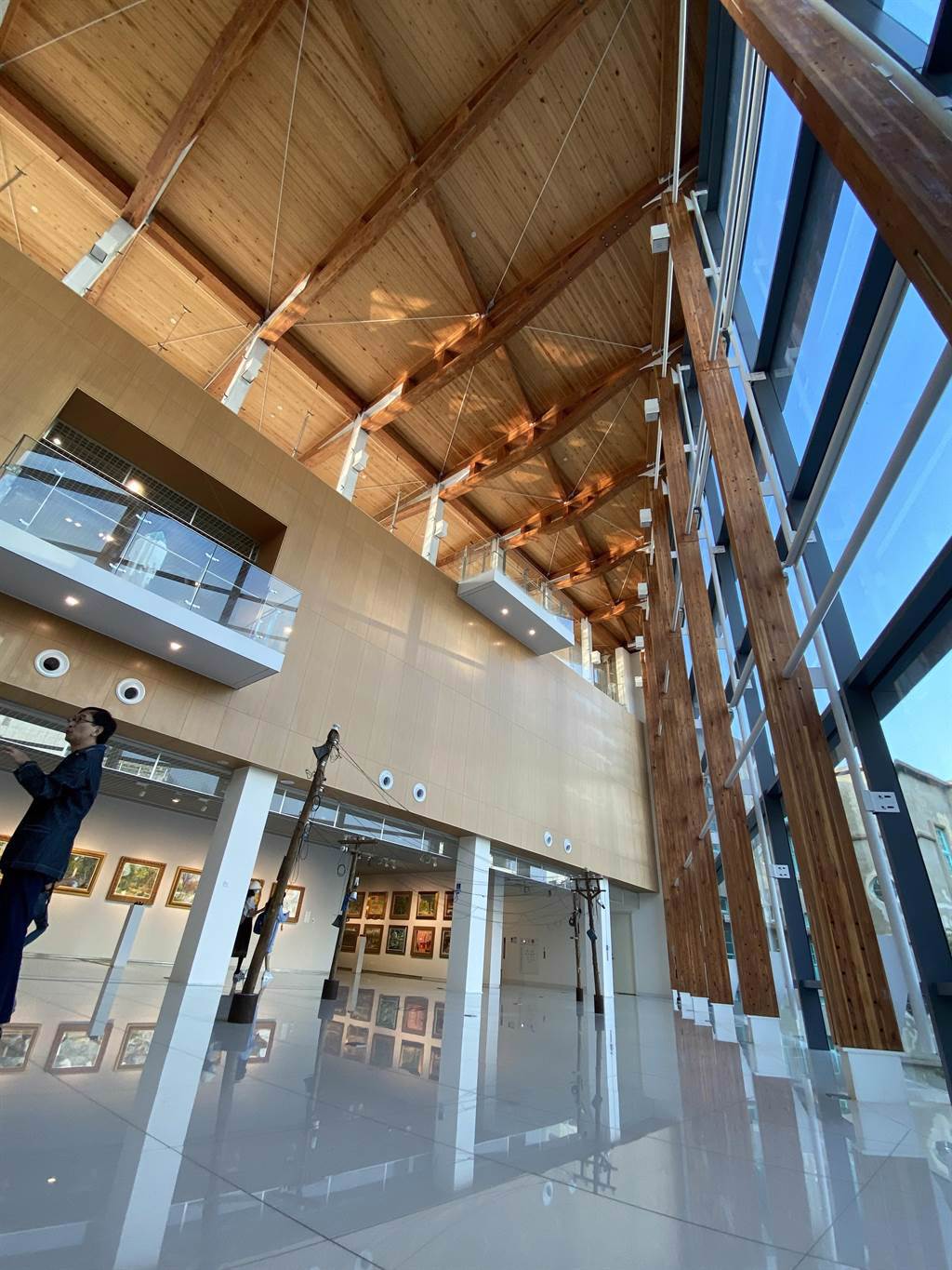 到嘉義美術館二樓，可以看到挑高的木構建築設計及大片的落地玻璃，大廳空間採用集成材樑柱而非鋼構，呼應嘉義作為「木都」的歷史特色。（馮惠宜攝）