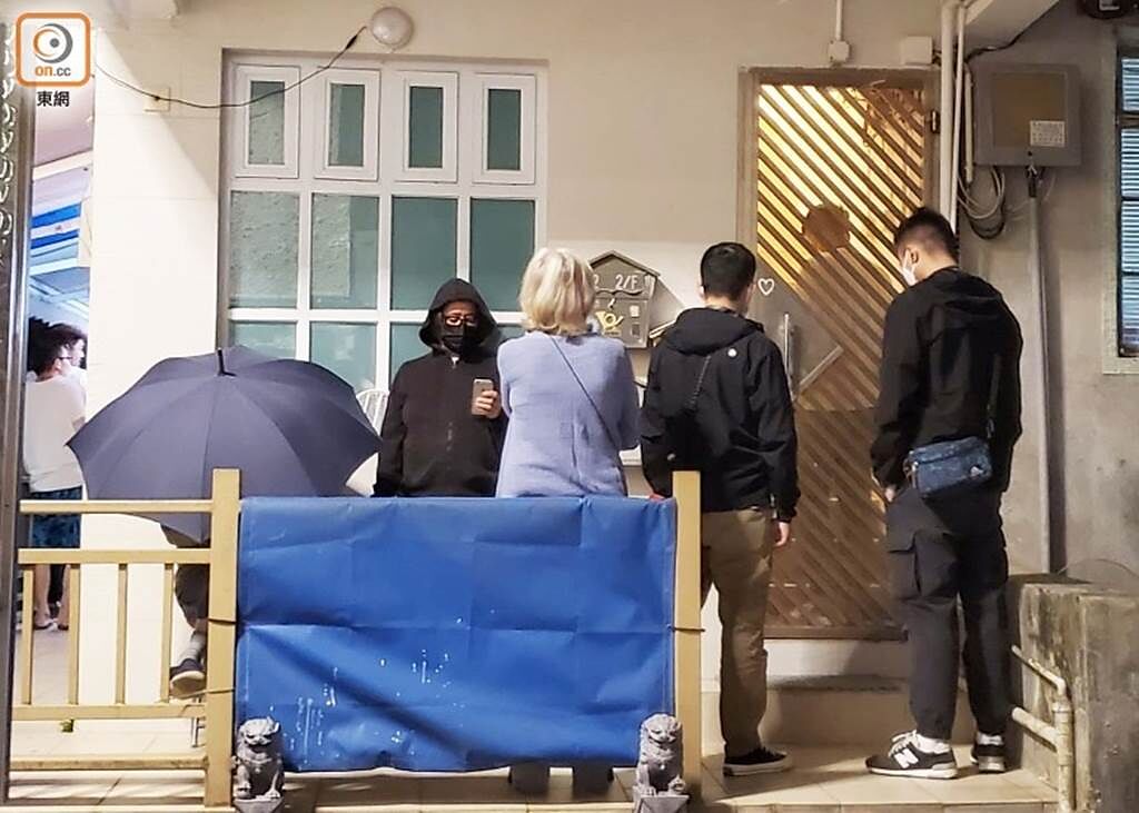 吳耀漢用雨傘遮擋，家人則在門旁等候消息。（圖／取自《on.cc東網》）