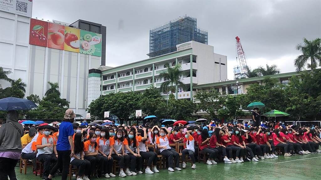 活動開始前現場突降大雨，集結於操場等待市長到來的學生，紛紛以雙手掩頭或脫下外套遮雨。（許哲瑗攝）