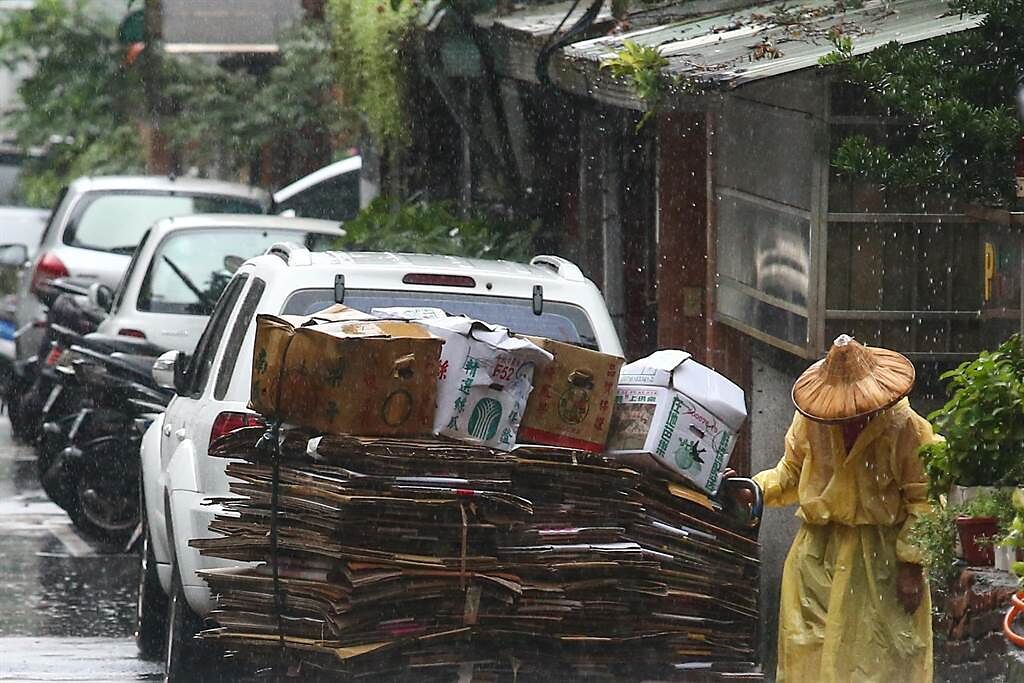滯留鋒面帶來雨量驚人，氣象局今(31)一度針對15縣市發布豪大雨特報。圖為一位婦人在大雨中，整理著被雨打溼的資源回收車。（鄧博仁攝）