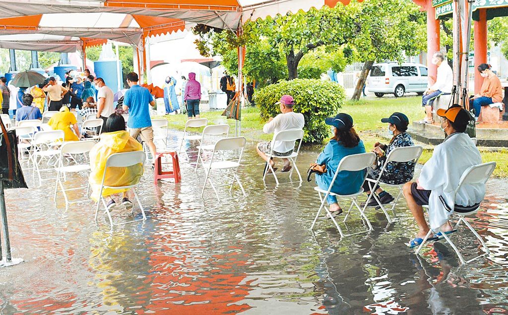 屏東枋寮國小篩檢站啟動首日因下起大雨，不少民眾泡在水裡，排隊等待篩檢。（林和生攝）