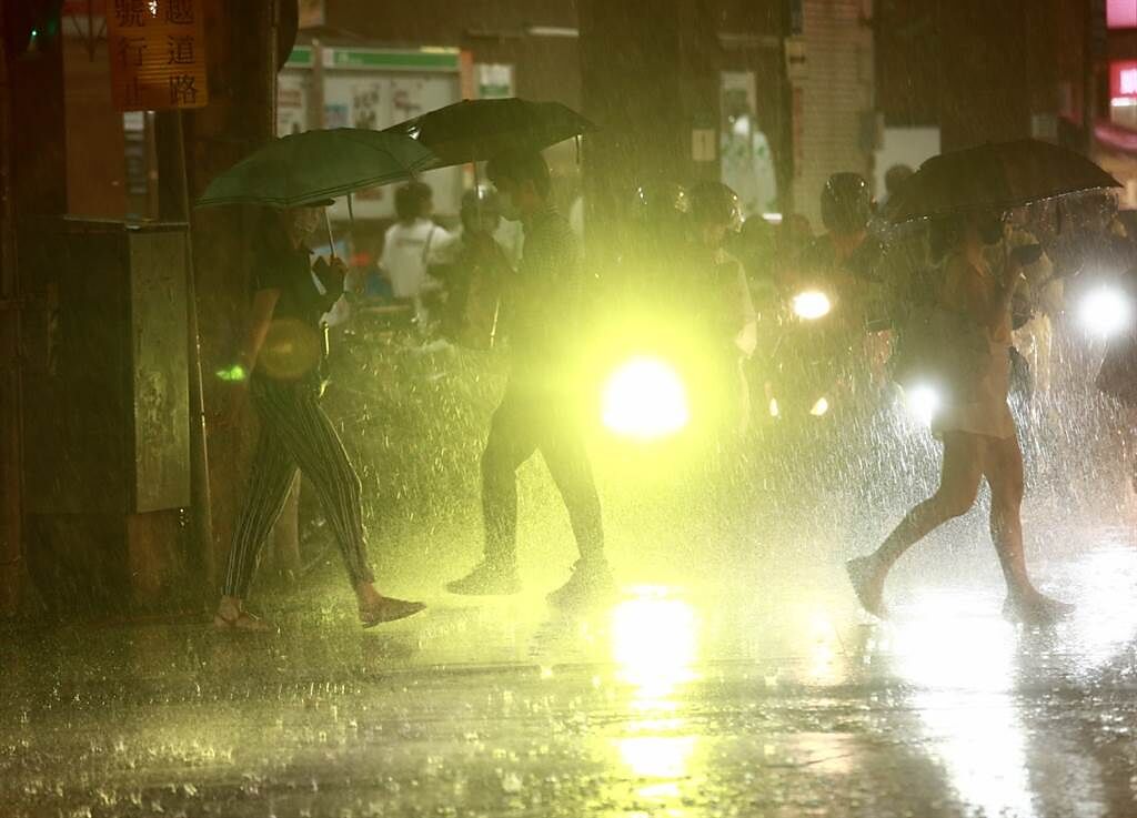 中央氣象局發布大雨特報，第6號颱風烟花外圍環流影響，北台灣天候不穩，晚間新北市突然下起大雨，下班民眾在大雨中穿越車陣。（陳信翰攝）