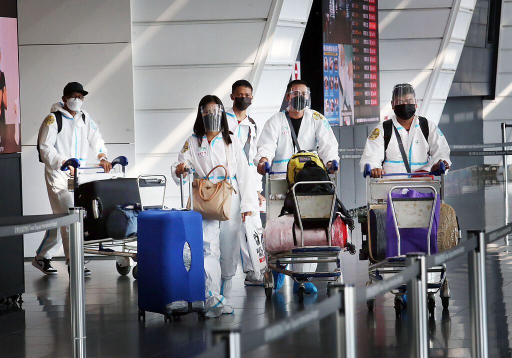 在桃園機場第一航廈入境大廳內，身穿防護衣的旅客準備搭車離開，清潔人員在後方消毒環境。（資料照/范揚光攝）