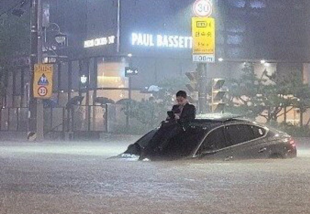 韓國一名男子在暴雨中坐車頂滑手機。（圖／翻攝推特@carryurlife2）