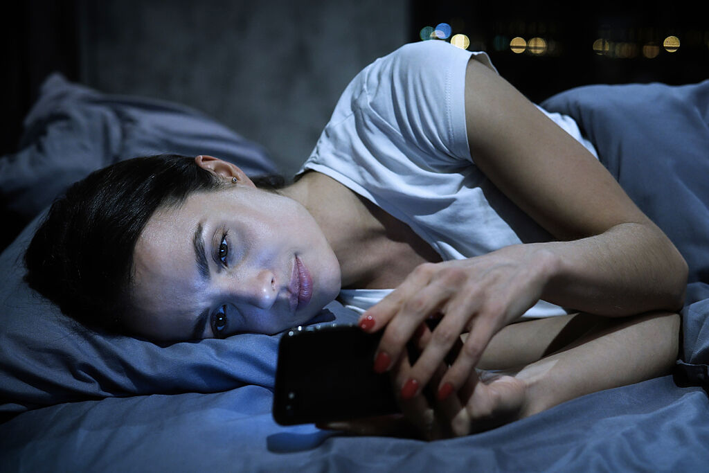 為紓解白天工作壓力，許多人習慣睡前滑手機看影片。(示意圖/ Shutterstock )