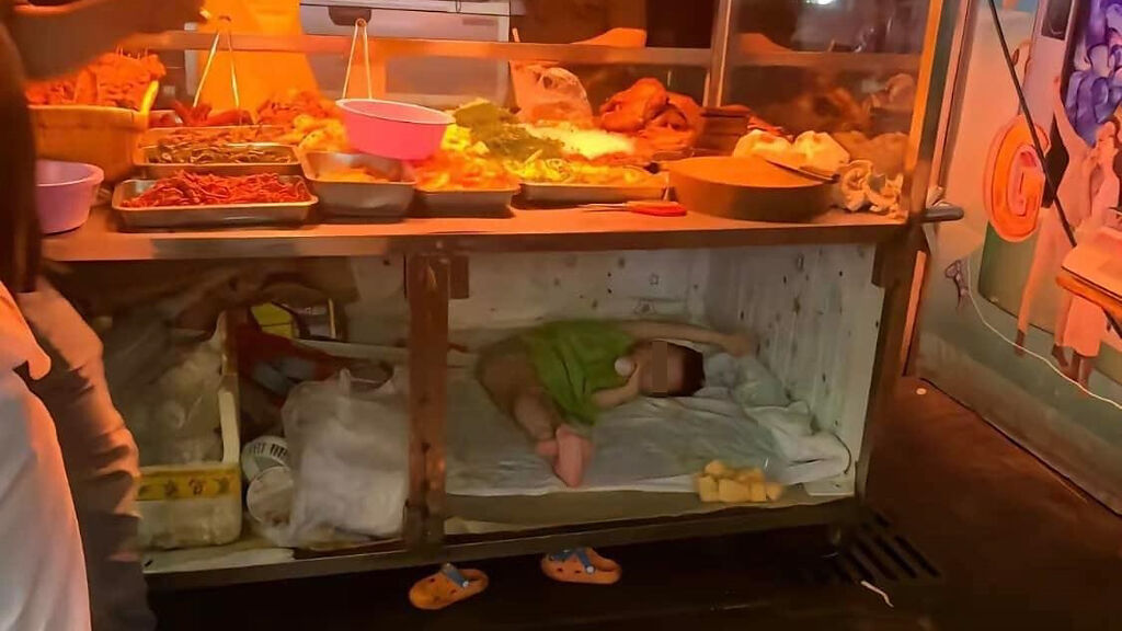 一對父母在路邊經營熟食攤車，攤車下方的櫃子躺了一名正在喝奶、約3歲大的男童。（圖／翻攝自CoNsの少男時代經典愛情語錄臉書粉專）